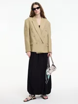 Blazer cruzado de color beige claro, con solapas anchas y doble hilera de botones frontales. Presenta bolsillos de solapa en la parte inferior.