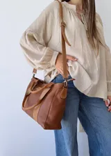 Bolso tipo tote de cuero color marrón con doble asa corta y correa larga extraíble.