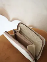 Billetera Actitud Sur de cuero con pelo vacuno en color blanco, con cierre perimetral y compartimentos internos de cuero.