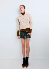 Chaqueta de punto color beige, de corte corto, con cuello camisero, bolsillos frontales con solapa y botones metálicos.