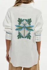 Camisa de lino blanca con cuello camisero, manga larga y puños con botones y detalles bordados. En la espalda presenta un gran bordado colorido con diseño de libélula y hojas.
