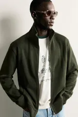 Chaqueta regular fit de cuello subido, confeccionada en tejido técnico interlock de algodón con elasticidad. Presenta cierre frontal con cremallera, manga larga con puños en rib y bolsillos de vivo en la cadera.