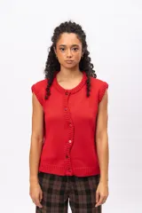 Chaleco de punto color rojo, sin mangas, con cuello redondo y cierre frontal asimétrico con botones. Presenta un diseño tejido con textura acanalada en los bordes.