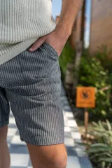 Bermuda de lino imperial a rayas verticales blancas y grises, con bolsillos laterales y traseros y elástico en la cintura.