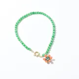 Collar corto de cuentas redondas color verde claro, con dije de flor naranja con centro negro y blanco. Cierre de mosquetón dorado.