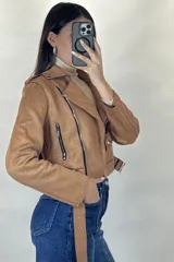 Chaqueta corta tipo biker confeccionada en gamuza color beige, con cierre frontal cruzado, solapas amplias, bolsillos con cierre y cinturón ajustable en la cintura.