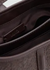 Bolso tipo bucket de tamaño pequeño, confeccionado con tejido de rafia color marrón con efecto texturizado y detalles en cuero sintético liso del mismo tono. Cuenta con un asa corta superior, herrajes metálicos dorados, cierre de imán y un detalle decorativo con candado dorado en la parte frontal.