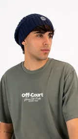 Gorro tipo beanie de punto acanalado en color azul marino, con detalle de parche circular con logo en la parte frontal.