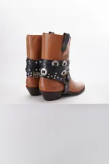 Bota de cuero color marrón con puntera fina y taco bajo. Presenta correas de cuero negro con apliques metálicos plateados.