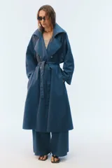 Trench coat oversize color beige, largo, con doble botonadura, solapas amplias, bolsillos laterales y cinturón ajustable para anudar.