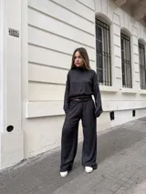 Conjunto de dos piezas compuesto por un buzo de cuello alto y mangas largas con diseño holgado, y un pantalón a juego. Ambas prendas están confeccionadas en tejido morley elastizado de color negro con un sutil efecto jaspeado.