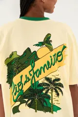 Camiseta Ipanema de manga corta en color amarillo pastel, con cuello redondo en contraste de color verde oscuro. Presenta un pequeño estampado en el pecho con diseño de escudo y palmeras.