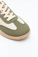 Zapatilla urbana de mujer con silueta retro, combinando paneles de cuero blanco y gamuza gris claro. Posee un talón trasero en gamuza negra y suela robusta de goma color caramelo con relieve.