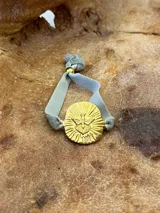 Pulsera con banda de terciopelo verde oliva y dije circular dorado con figura de paloma y rayos.