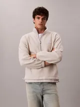 Buzo polar de Calvin Klein en color beige, con cuello alto tipo mock neck y cierre de media cremallera frontal. Presenta un diseño de corte regular con mangas largas, bajo ajustable con cordón y logo de la marca bordado en el pecho.