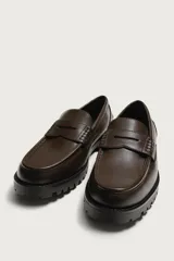 Mocasín de vestir negro con capellada lisa, detalle de antifaz en el empeine y suela track robusta.