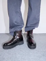 Bota corta de cuero negro tipo biker, con suela track de goma, plataforma, costuras y bordados decorativos en hilo rojo. Presenta tiras con hebillas metálicas y cierre en la parte trasera.
