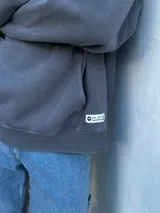 Buzo canguro gris con capucha y cordón ajustable, bolsillo tipo canguro y puños y cintura acanalados.