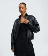 Campera estilo bomber de cuero sintético (PU) color negro, con cuello alto estructurado, cierre frontal con cremallera y botones a presión, mangas largas y detalle de cinturón ajustable en la cintura.