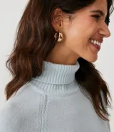 Suéter de tejido de punto color beige con cuello alto, mangas con corte raglán y puños y ruedo acanalados. Presenta un diseño clásico y cómodo con el ruedo trasero ligeramente más largo.