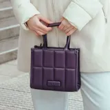 Cartera tote chica color púrpura, con diseño acolchado y logo metálico XL al frente. Tiene doble asa corta y correa larga regulable.