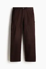 Pantalón estilo carpenter de sarga de algodón, color marrón oscuro, con corte recto y costuras reforzadas en las rodillas. Presenta bolsillos laterales, bolsillo monedero, bolsillos traseros, trabilla lateral y bolsillo cargo con doble compartimento.