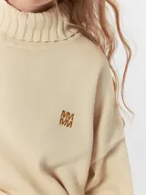 Pullover de punto color rojo, con cuello tortuga, corte holgado y mangas largas con puños acanalados en contraste con rayas blancas. Presenta un logo bordado en el pecho.