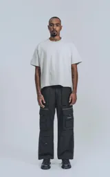Pantalón cargo negro de silueta oversize, confeccionado en tejido técnico liviano de poliéster. Presenta múltiples bolsillos cargo con solapa y detalles reflectivos horizontales en la parte superior de los bolsillos.