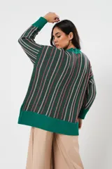 Sweater verde esmeralda de cuello redondo y manga larga, con terminación acanalada en puños y ruedo. Presenta tajos laterales y diseño de rayas verticales en tonos blanco y rosa.