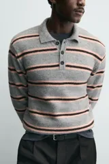 Polo de punto de corte relajado con diseño de rayas horizontales en tonos gris, rosa y marrón. Presenta cuello solapa, cierre frontal con botonadura y mangas largas con puños acanalados.