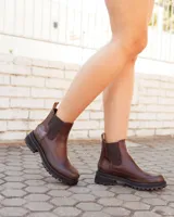 Botas tipo Chelsea de cuero color chocolate, con paneles elásticos laterales, suela track dentada y detalle de textura en el talón.