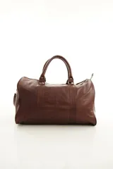 Bolso de viaje color marrón, confeccionado en cuero vacuno, con doble asa de mano y correa ajustable y desmontable. Cuenta con herrajes metálicos y costuras reforzadas.