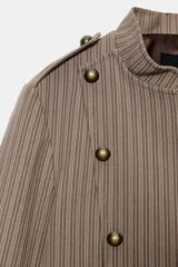 Blazer entallada color beige con rayas verticales finas, cuello redondo y manga larga. Presenta trabillas en los hombros y botones metálicos decorativos en el frente. Cierre frontal con cremallera y forro interior.