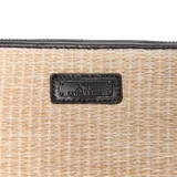 Billetera tipo fichero de diseño trenzado en tono natural, con bordes y detalles en cuerina negra. Posee cierre perimetral y placa metálica frontal con el logo grabado.