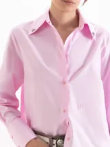 Camisa holgada de poplin blanco, con cuello clásico, mangas largas con puños anchos y cierre frontal con botones. Presenta detalles de apliques metálicos en las puntas del cuello y sutil bordado en el delantero.