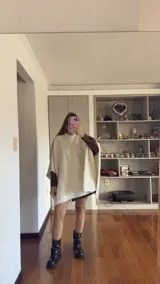 Poncho de tejido de punto en color beige, con cuello alto y diseño holgado sin mangas.