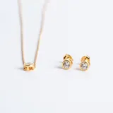 Set de joyería compuesto por un collar con dije de punto de luz y un par de aros tipo caravanas a juego. Ambas piezas presentan circonias engarzadas en bases circulares con baño de oro.