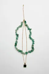 Collar doble dorado, compuesto por una cadena corta con piedras en bruto de color verde y una cadena más larga con dije cuadrado de piedra verde.