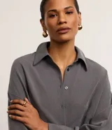 Camisa gris de tejido plano con corte sastre, cuello clásico, abotonada en el frente y puños largos.