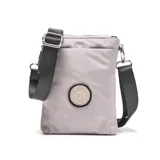 Bandolera mini color gris claro, de formato compacto rectangular. Cuenta con doble compartimento con cierre superior, correa larga regulable negra y herrajes metálicos color níquel. Tiene un bolsillo interno y un logo circular en el frente con la inscripción "Extra Large".