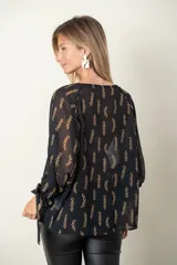 Blusa negra de gasa con estampado de cadenas doradas, escote redondo y mangas largas abullonadas con lazos en los puños.