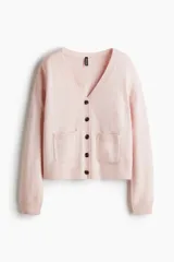 Saco de punto suave color rosado, con cuello en V y cierre frontal de botones. Diseño de corte holgado con hombros caídos, bolsillos delanteros abiertos y remate acanalado en puños y bajo.