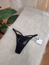 Tanga de encaje negro con diseño de tiras laterales regulables y detalle de transparencia. Cuenta con refuerzo de algodón en la entrepierna.