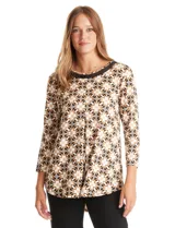 Blusa de seda fría estampada con un patrón geométrico en tonos blanco, negro y marrón. Presenta un escote redondo con detalle de transparencia y un ribete trenzado negro con un aplique dorado. Tiene mangas tres cuartos y un corte fluido con una pequeña tabla central que crea un drapeado suave. El ruedo es redondeado y ligeramente más largo en la parte posterior.