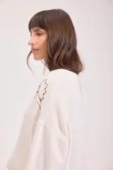 Sweater de punto color negro, de corte holgado y manga larga, con detalle de bordado calado en los hombros y a lo largo de las mangas.