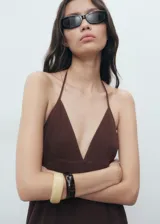 Vestido midi marrón de 100% algodón, sin mangas, con escote en pico y tirantes finos que se atan al cuello. Presenta diseño evasé con detalles fruncidos escalonados y textura.