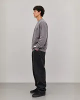 Buzo oversize de cuello redondo en color gris, con diseño estampado en el frente que incluye logotipos y texto. Presenta puños y ruedo acanalados, con una pequeña etiqueta decorativa en la parte inferior.