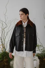 Camisa marrón de cuero sintético con cuello de piel sintética color marrón, cierre frontal con botones a presión dorados, dos bolsillos con solapa en el pecho y corte holgado.