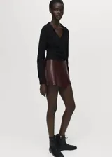 Falda pantalón corta de efecto piel en color bordó, de tiro medio y diseño cruzado con cierre de cremallera lateral.
