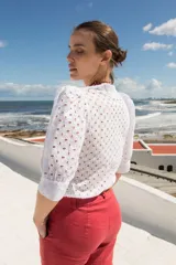 Camisa de estilo romántico confeccionada en tela broderie blanca, con mangas al codo abullonadas y cierre frontal con botones.